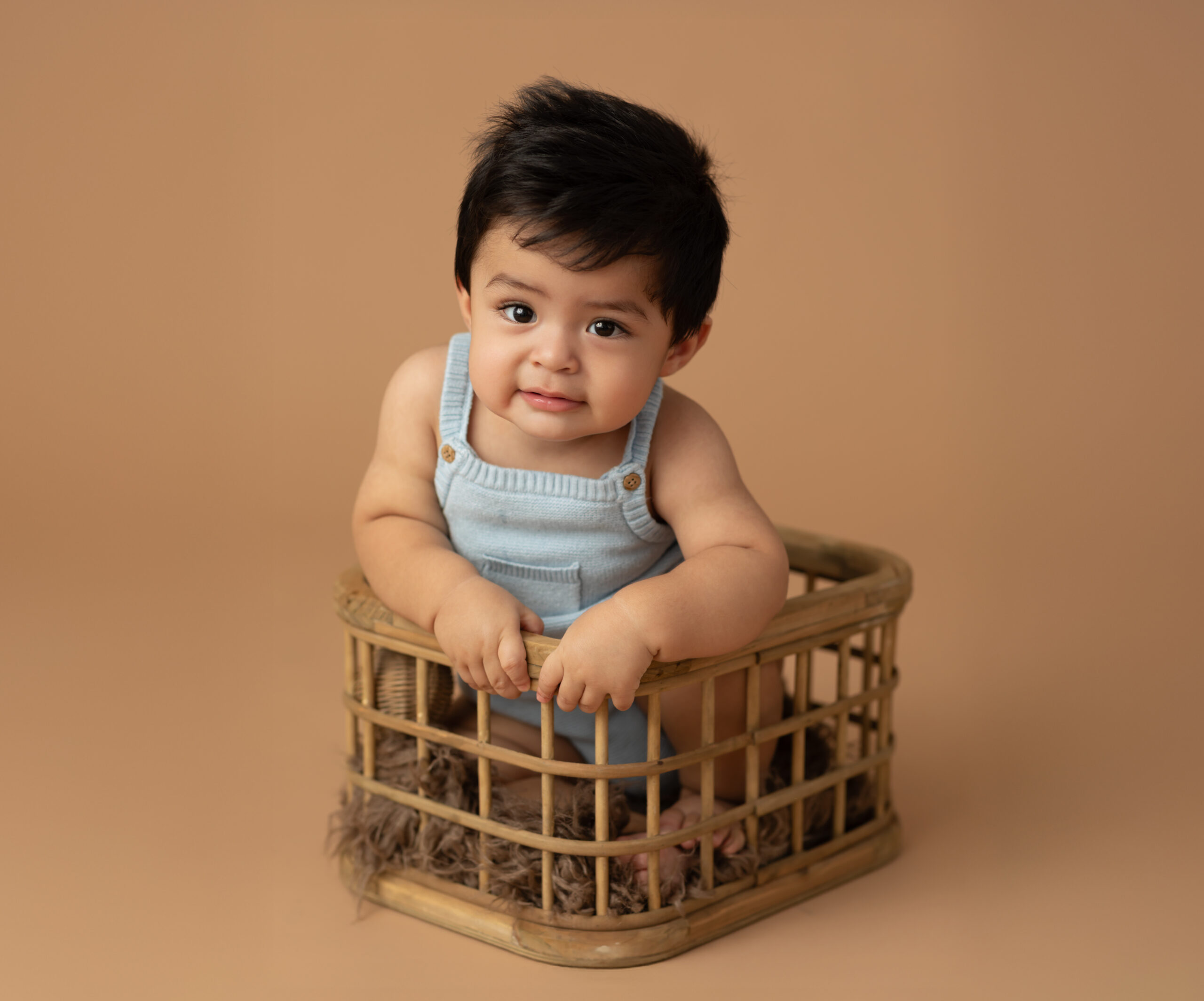 one year old boy in blue onesie sitting in basket for milestone portraits Swim Lessons in Cleveland Ohio