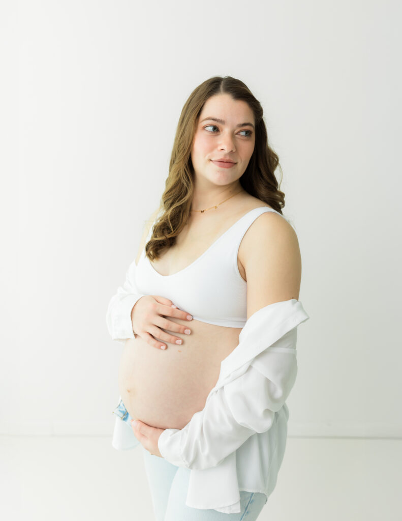 pregnant mother in white bra and jeans holding baby bump for maternity photoshoot Prenatal yoga Akron